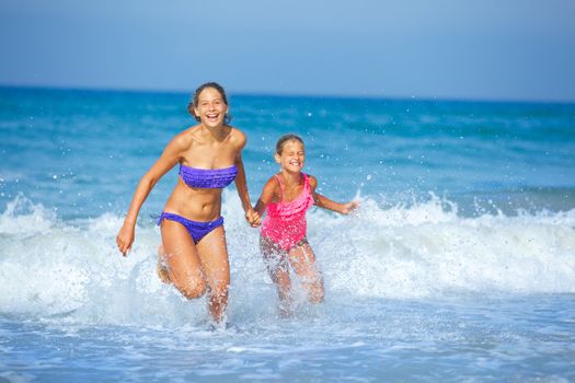 Cute girls friends running together in the beach shore on summer vacation