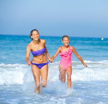 Cute girls friends running together in the beach shore on summer vacation