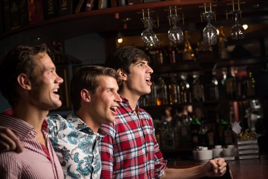 Three men stand in a row embracing smile and look in front of you, sports fans