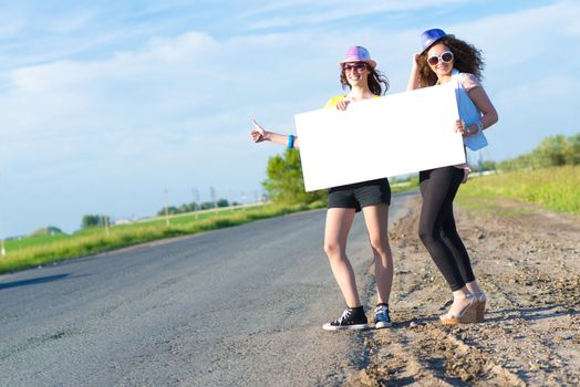 Two young women stand with a blank banner on the side of the road, place for text