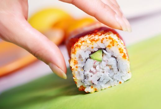 Close-up horizontal photo of the human hand taking rolled sushi with cucumber rice tuna and caviar. Shallow depth of field