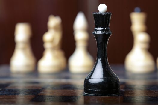 Chess game. Black queen against the group of white cheesmen. Close-up horizontal photo