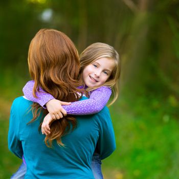Mum holding daughter kid girl in her arms rear view smiling in outdoor