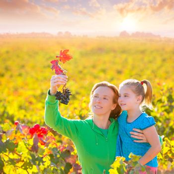 Mother and daughter family on autumn vineyard happy smiling holding grape bunch