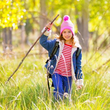 Hiking kid girl with backpack in autum poplar trees forest and walking stick