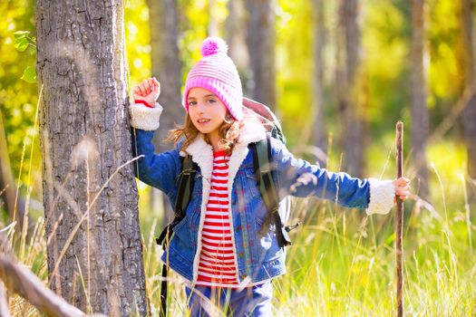 Hiking kid girl with backpack in autum poplar trees forest and walking stick