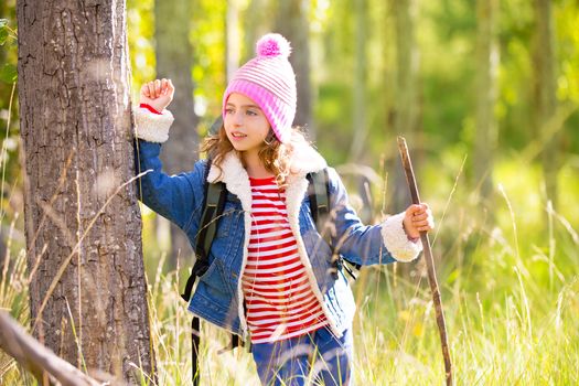 Hiking kid girl with backpack in autum poplar trees forest and walking stick