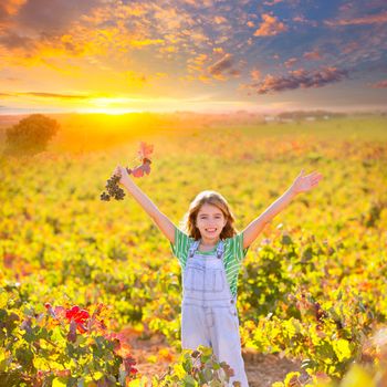 Kid girl in happy autumn vineyard field open arms with red leaf grapes bunch in hand