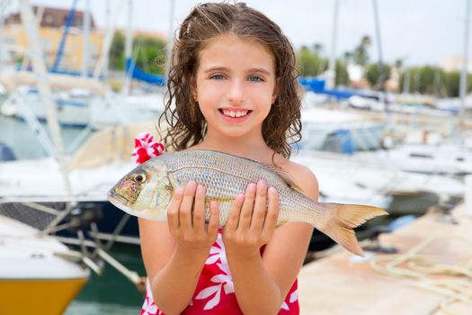 Happy kid fisherwoman with dentex fish catch in Mediterranean marina
