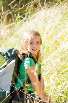 Blond explorer kid girl walking with backpack between forest grass