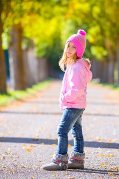 autumn winter kid girl blond with jeans and pink snow cap in trees track