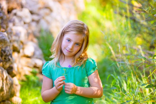 Blond kid girl smiling with purple flower relaxed in green outdoor