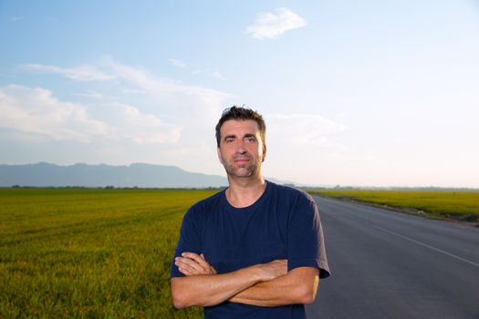 Mid age man in road at meadows posing with crossed arms cereal fields