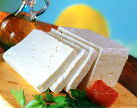 Sliced feta cheese on wooden cutting board with olive oil aside.