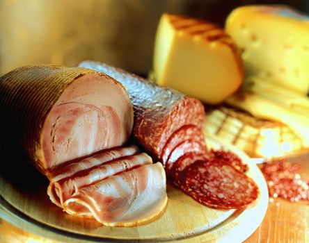 Variety of cheeses  and cold cuts on wooden board.