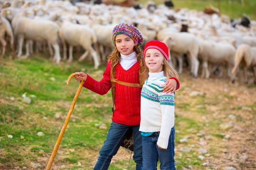 Kid girl shepherdess sisters happy with flock of sheep and wooden stick in Spain