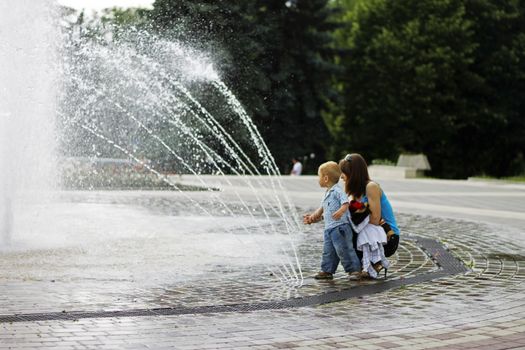 Woman and child walking around splashing fontain in the center of the town