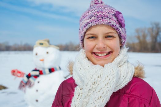 Close-up portait of happy beautiful girl with snowman outside in winter time