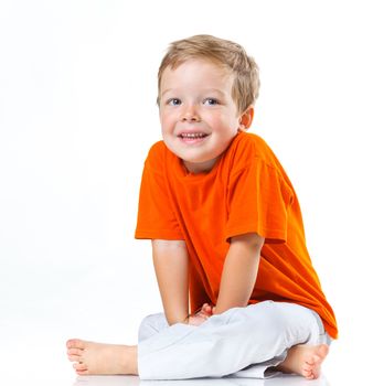 Adorable happy boy sitting on the floor in studio. Isolated of white background.