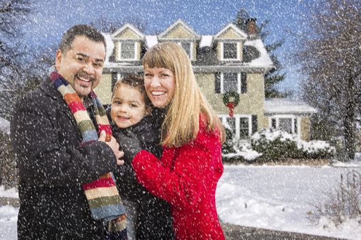 Happy Mixed Race Young Family in Front of Beautiful Snow Covered House While Snow is Falling.