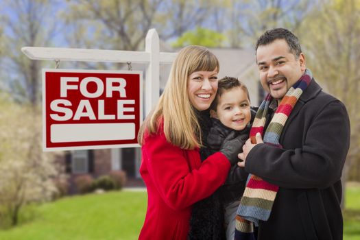 Warmly Dressed Young Mixed Race Family in Front of Home For Sale Real Estate Sign and House.