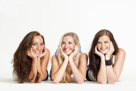 three young female friends lying on the floor, looking ar camera, smiling