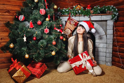 Attractive young woman holding gift and sits near Christmas tree