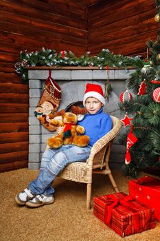 Boy sitting in wicker chair near Christmas tree on background of fireplaces