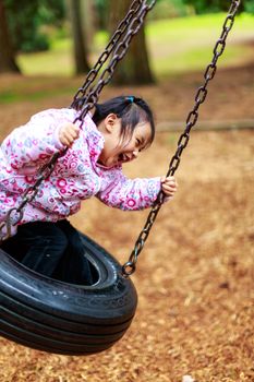 A little girl having a great time on a swing in a playground.