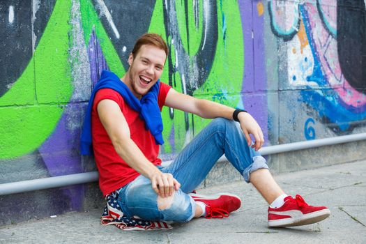 Happy teens boy sitting near painted wall and having fun