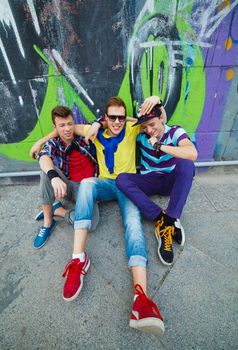 Happy three teens boy sitting near painted wall.
