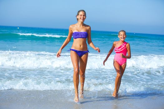 Cute girls friends running together in the beach shore on summer vacation