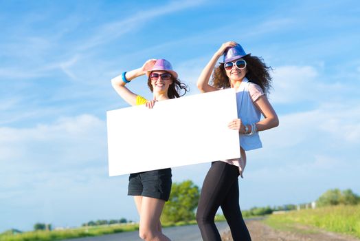 Two young women stand with a blank banner on the side of the road, place for text