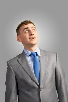 portrait of a young businessman thinking and looking up on gray background