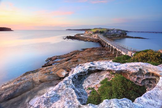 Bare Island Australia, view from La Perouse, Sydney bathed in pretty pastel pink and yellow light at sunrise on a calm summers morning. Focus to foreground.