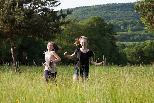 Two teens girls running in tall grass on a meadow