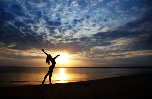 Lady doing exercise at the beach during sunset. Vivid colors and natural darkness