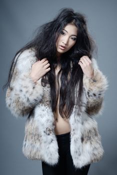 Asian beauty in fur coat posing in the studio