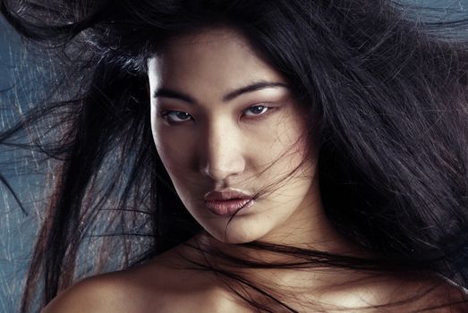 Portrait of the sexy Asian witch with blowing hairs and bronze skin