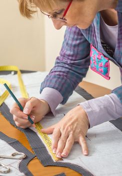 Woman dressmaker drawing tailor pattern with pencil for a suit on the table