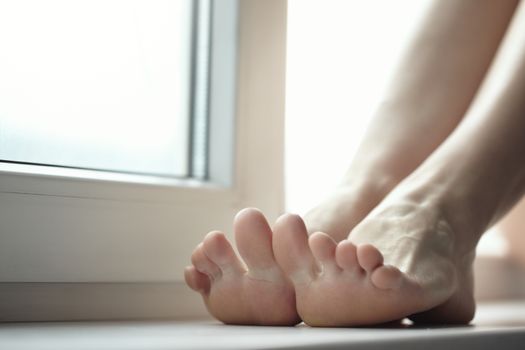 Feet of the woman sitting on windowsill. Close-up horizontal photo with shallow depth of field for natural view
