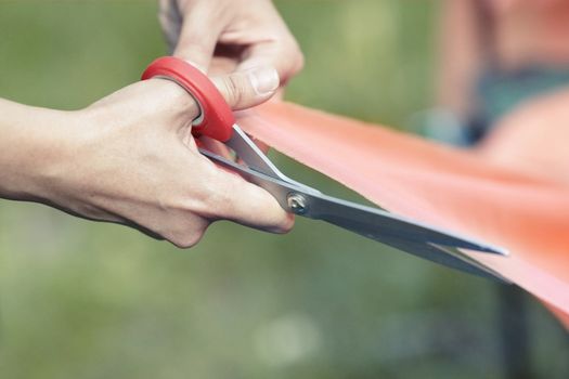 Hands of female tailor cutting red ribbon. Close-up view