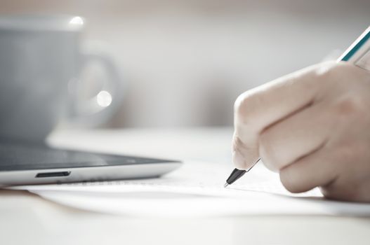 Human hand with pen calculating budget. Teacup and digital tablet on a table