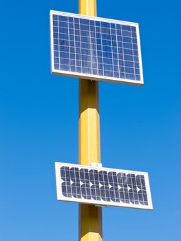 Solar electric panels mounted on yellow pole providing off-grid power in full sun against blue sky