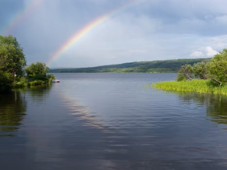 Rainbow over calm water of northern boreal forest taiga lake, northern British Columbia, Canada