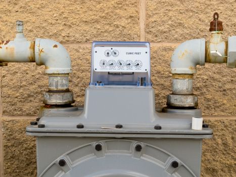 Residential natural gas meter on exterior wall to measure household energy consumption shows reading on dial display