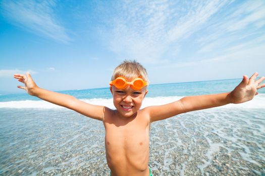 Playful boy in swimming goggles on the beach with sea on background