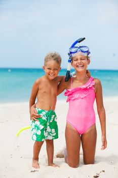 Two happy children on beach with colorful face masks and snorkels, sea in background.