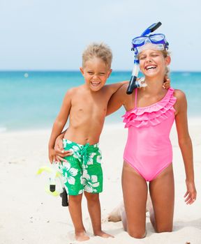 Two happy children on beach with colorful face masks and snorkels, sea in background.