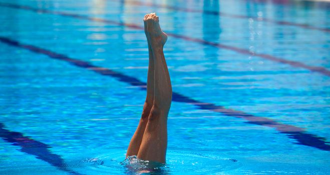 Synchronized swimmers legs point up out of the water in action